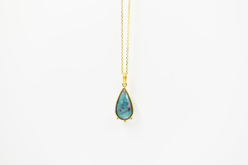 Teardrop-shaped turquoise pendant on a gold chain against a white background