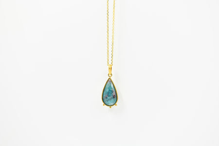 Teardrop-shaped turquoise pendant on a gold chain against a white background