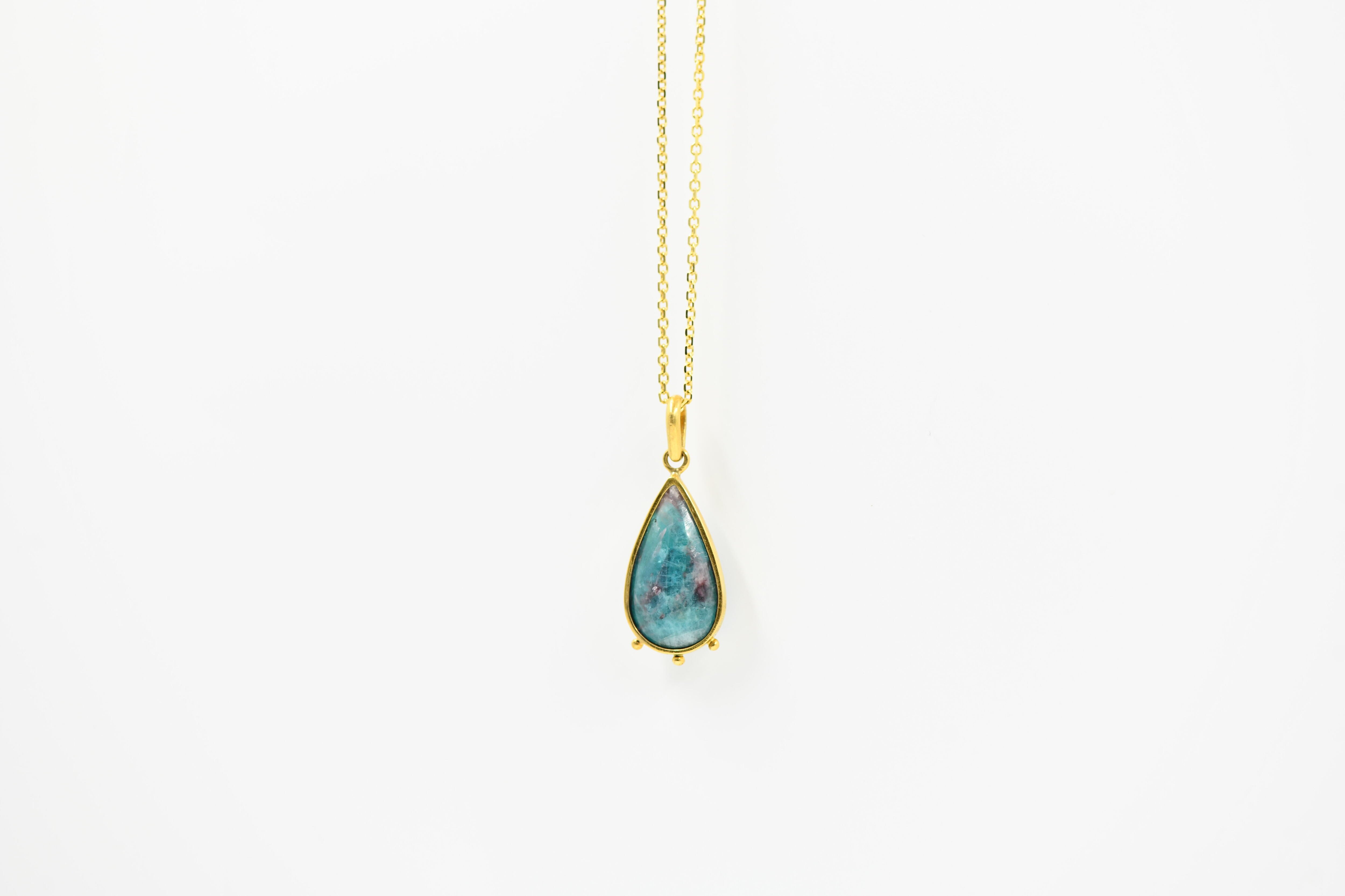 Teardrop-shaped turquoise pendant on a gold chain against a white background